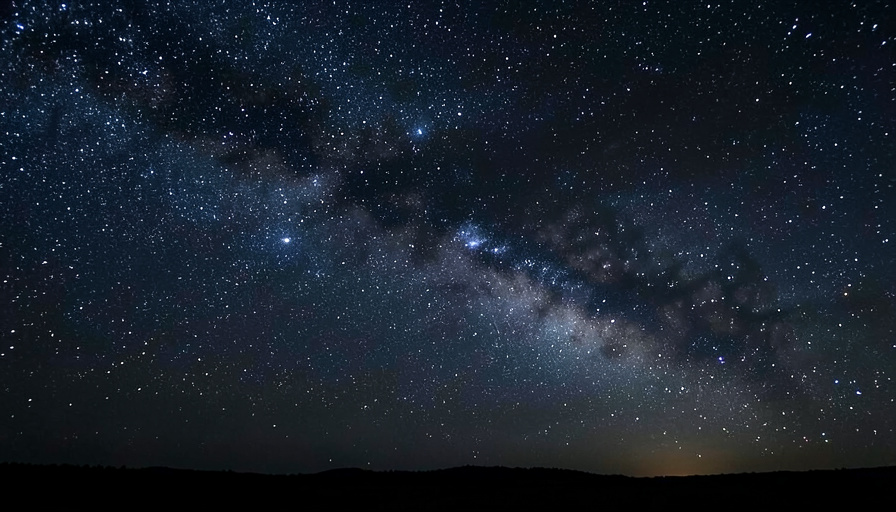 The Milky Way arching as a glowing band of stars and dust across the night sky above a dark horizon, our view from inside our own galaxy