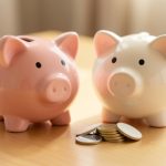 A ceramic piggy bank beside a small stack of coins on a clean wooden desk in warm soft light