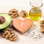 Heart-healthy foods including avocado, salmon, walnuts, olive oil and oats arranged around a small heart shape on a table